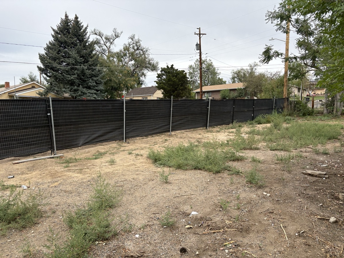 Tribute Fencing & Barricade temporary construction fencing with black privacy windscreen, posts driven into the ground around a vacant lot